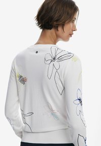 Maglione bianco con ricami floreali in vari colori. Classico scollo rotondo, orlo a costine e un piccolo dettaglio con il logo sul retro.