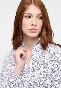 Wei�ße Bluse mit einem marineblauen, abstrakten Wirbelmuster, aus leichtem Stoff, mit Kragen und Knopfdetails, und teilweise zurückgerollten Ärmeln.
