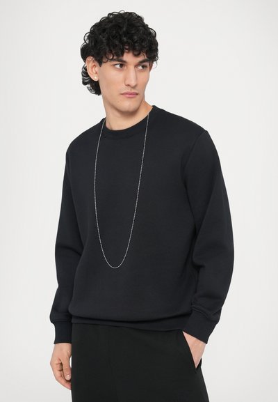 Μαύρο φούτερ με στρογγυλή λαιμόκοψη, μακριά μανίκια και ριμπ τελειώματα. Διαθέτει ασημένιο αλυσίδα κολιέ και διακριτική λεπτομέρεια λογοτύπου στο στήθος.