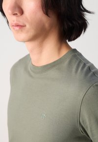 T-shirt en coton olive avec un encolure ronde, des manches courtes et un petit logo brodé sur la poitrine. Texture lisse.