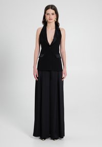 Schwarzes Vestkleid mit tiefem V-Ausschnitt, satinartigen Revers und seitlichen Taschen. Es fließt zu einem langen, geplauten Rock und zeigt eine glatte Textur.