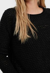 Maglione nero lavorato a maglia con un motivo strutturato, scollatura rotonda e maniche lunghe, caratterizzato da una vestibilità ampia e dettagli sottili.