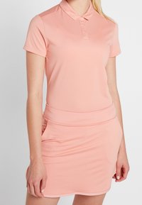 Polosové šaty v jemně růžové barvě, vyrobené z prodyšné látky. Mají límeček, krátké rukávy a na těle přiléhavý pas s vícevrstvým designem sukně.