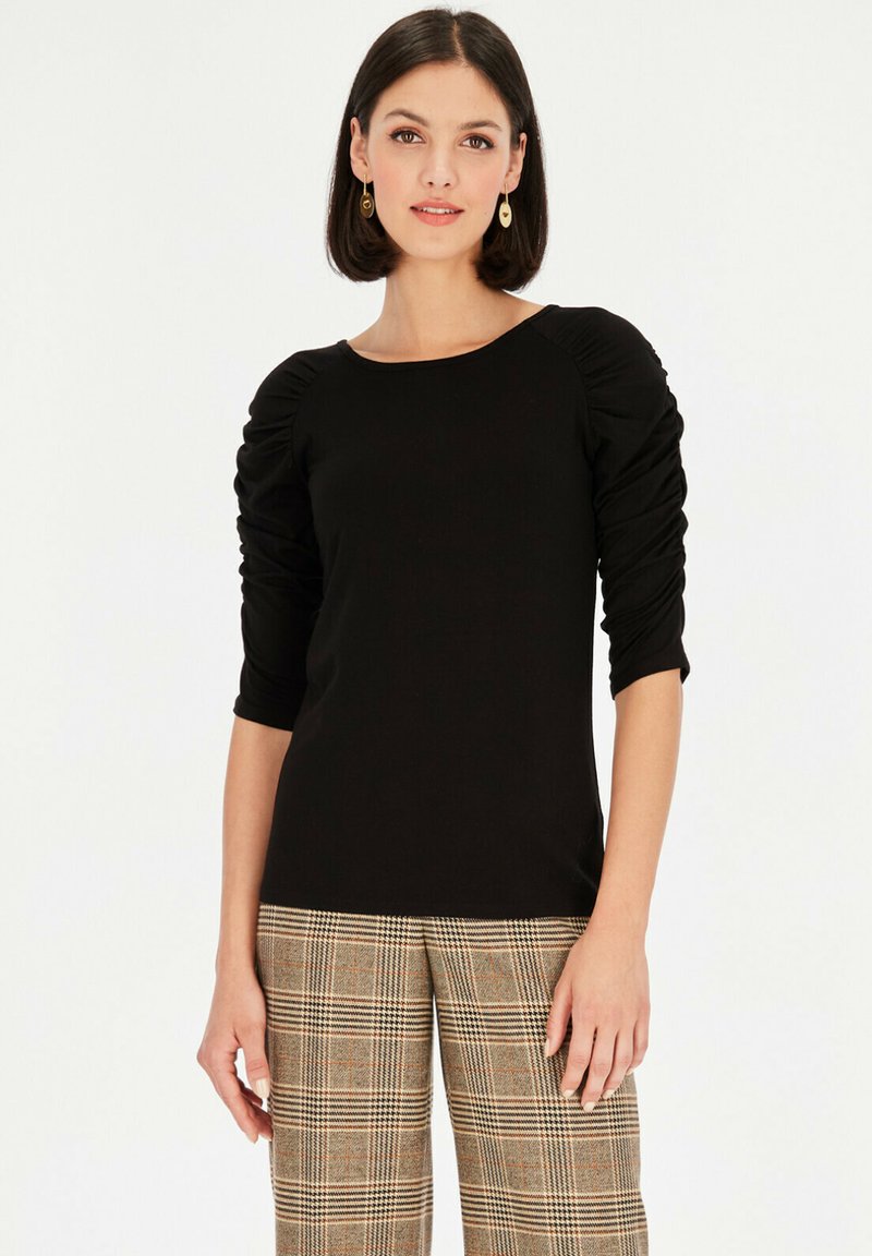 Czarny dopasowany top z półdługimi bufkami i okrągłym dekoltem, zestawiony z szerokimi spodniami w kratę z beżowymi i pomarańczowymi akcentami.