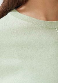 Pull léger vert avec un col rond côtelé et une texture lisse. Le tissu semble doux et légèrement extensible, sans motifs visibles.