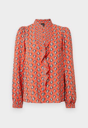Blouse rouge à manches longues, col à volants, imprimé géométrique en orange, noir et crème. Tissu léger à texture lisse.