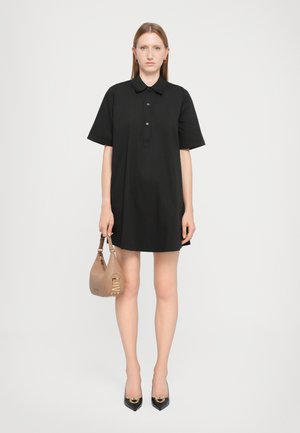 Schwarzes Polokleid mit kurzen Ärmeln, Kragen und Knopfdetails. Kombiniert mit einer hellbraunen, geschwungenen Handtasche mit goldener "LOVE"-Buchstabierung.