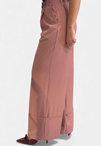 Pantaloni a vita alta e vestibilità ampia in rosa polveroso, realizzati in tessuto liscio. Presentano pieghe laterali e spacchi sull'orlo; abbinati a scarpe con punta appuntita.