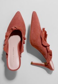 Ein Paar pinkfarbene Wildleder-Pumps mit spitzen Zehen und Rüschenkanten, von oben und von der Seite auf einem hellen Hintergrund gezeigt.