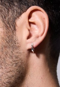 Srebrna kolczyk kołowy o eleganckim designie. Posiada lekko zakrzywiony kształt i trzy ostre akcenty. Noszony na lewym uchu.