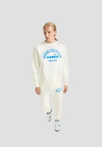 Felpa color crema e pantaloni abbinati, con stampa di testo blu, caratterizzati da collo rotondo, polsini elasticizzati e una vestibilità comoda.