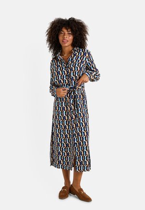 Robe longue et à motifs dans des tons de bleu, beige et marron. Présente un devant à boutons, une ceinture à la taille et des fentes sur les côtés pour faciliter les mouvements.