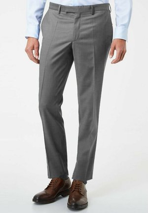 Pantalons de costume gris avec une coupe ajustée, présentant des plis à l'avant et une texture lisse. Associés à des chaussures en cuir marron à lacets.