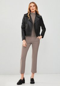 Zwarte leren motorjack met ritsaccenten, grijze coltrui en beige cropped broek. Zwarte loafers met dikke zool.