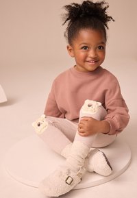 Ružová mikina, pruhované legíny s aplikáciami medveďov na kolenách, biele nadýchané papuče, textúrovaná tkanina a voľný strih.