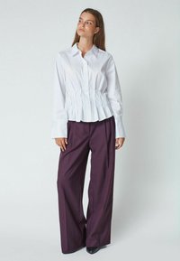 Chemise blanche boutonnée avec un design plissé à la taille, associée à un pantalon ample de couleur violet foncé. Tissu lisse et manches ajustées.