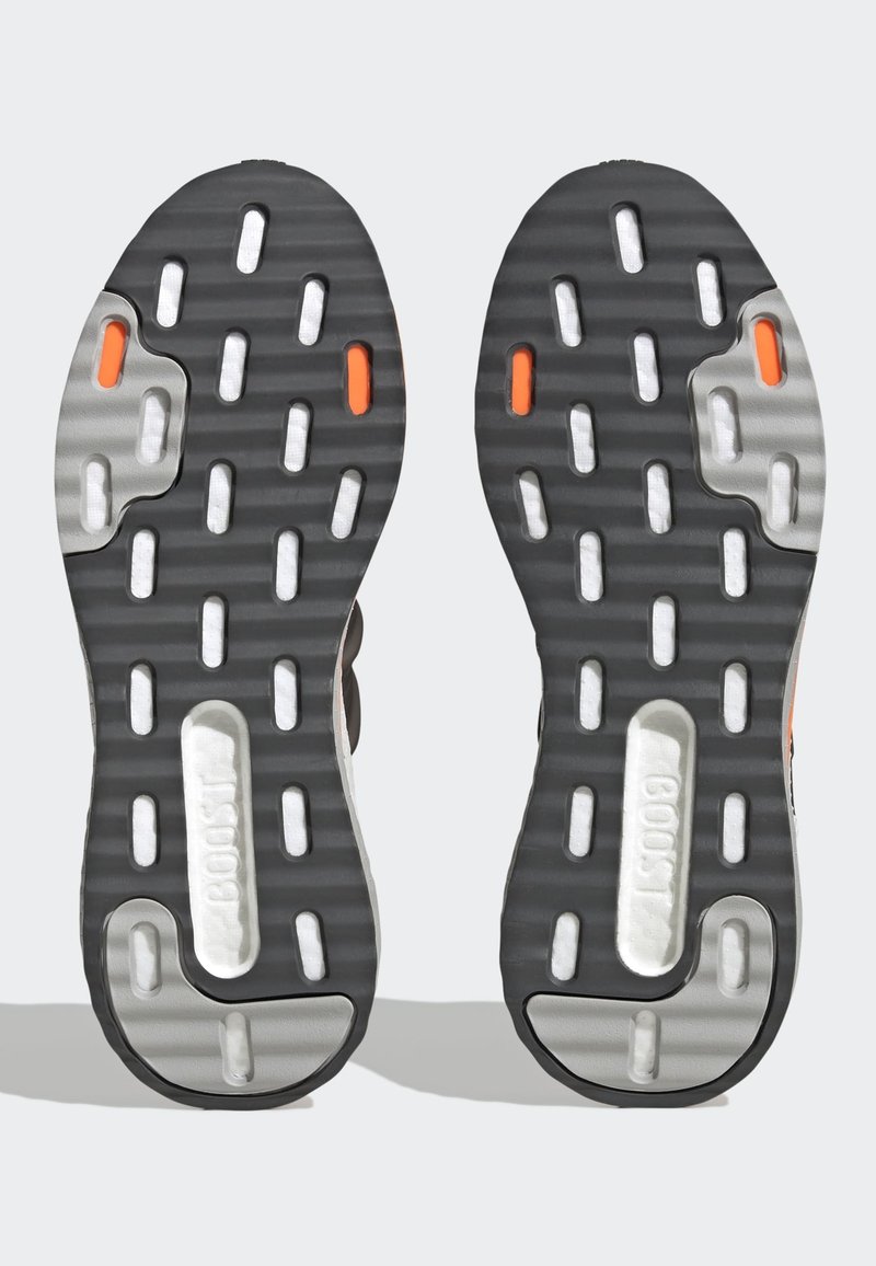 Suela de goma negra con patrones en blanco y gris, que presenta ranuras horizontales y acentos naranjas. Incluye el detalle del logo "BOOST".