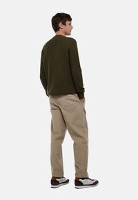Pull à côtes vert olive, pantalon en velours côtelé beige, baskets noir et blanc avec des accents rouges. Vue de dos, mains dans les poches.
