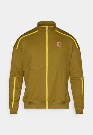 Alyvuogių spalvos zip-up treniruočių striukė su geltonomis detalėmis, turinti aukštą apykaklę, raukšlėtus rankogalius ir mažą logotipą ant krūtinės.