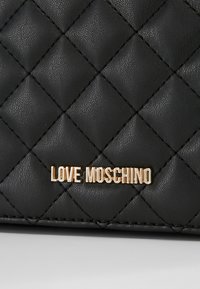 Černá prošívaná kabelka z umělé kůže s logem "LOVE MOSCHINO" ve zlatém tónu, s diamantovými vzory a dekorativním prošíváním.