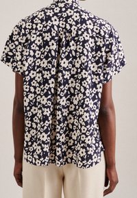 Kortärmad blommig skjorta med marinblå bakgrund, prydd med vita blommönster, något lös passform och detalj med plisséer i ryggen.
