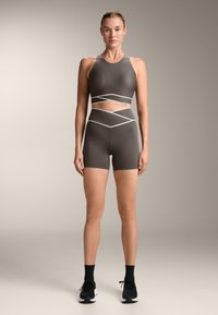 Atletski set, ki vsebuje temno sivo kratko majico z belimi poudarkom in usklajenimi visokimi kratkimi hlačami; gladek material, prilegajoča zasnova.