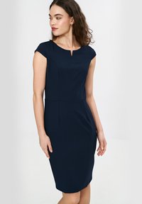 Granatowa sukienka bez rękawów z okrągłym dekoltem i subtelnym detalem w kształcie dziurki. Dopasowany krój z pionowymi szwami i długością do kolan.