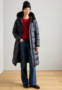 Zwarte pufferjas met een capuchon, met een ritssluiting en geribbelde manchetten. Draag over een rode trui en gecombineerd met uitlopende blauwe jeans en zwarte schoenen.