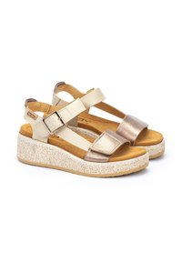 Sandalias de cuña en beige y dorado metálico con correas elásticas, hebillas y suelas texturizadas similares al corcho. Diseño minimalista con punta abierta.