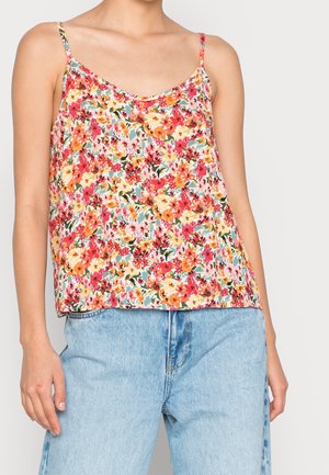 Femme portant un débardeur sans manches à imprimé floral avec de fines bretelles et un jean taille haute bleu clair, sur un fond uni.