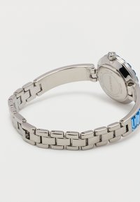 Ασημένιο ρολόι από ατσάλι, με συνδεδεμένο μπρασελέ, διακοσμητικά από μπλε κρύσταλλο και ανοιχτό κούμπωμα σε λευκό φόντο.