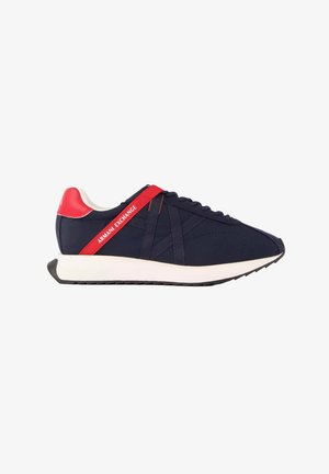 Zapatilla deportiva azul marino con suela blanca, talón rojo y correa con etiqueta Armani Exchange en el lateral, vista desde el exterior.