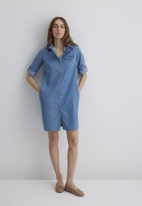 Denim shirt dress with a button front, short rolled sleeves, two chest pockets, and a relaxed fit. Light blue color, knee-length.