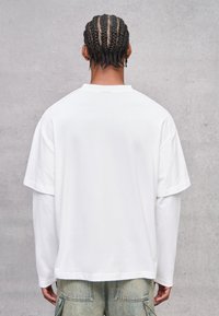 Weißes, übergroßes T-Shirt mit kurzen Ärmeln, weichem Baumwollstoff und Rundhalsausschnitt, von hinten vor einem neutralen Hintergrund gezeigt.