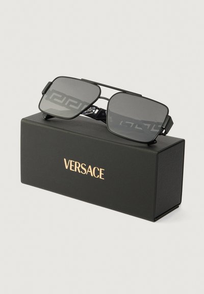 Kvadrātveida melni saulesbrilles ar pelēkiem stikliem, metāla rāmis, un Versace logo uz melnas kastes ar zeltaini burtiem. Kastei ir vienmērīga tekstūra.