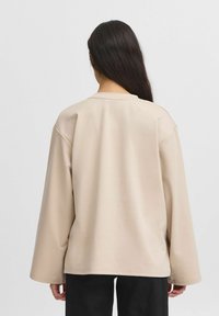 Beige pullover-sviiter, millel on pikad varrukad, ümar kaelus ja mugav lõige. Sile tekstuur, ilma nähtavate mustriteta või kinnitusteta. Näha on mustad püksid.