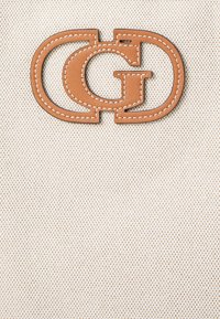 Beige szövet háttér egy nagy, dombornyomott barna bőr logóval, amely összekapcsolt 'G' betűket ábrázol, fehér varrással kiemelve.