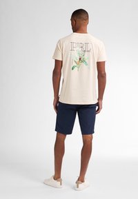 Camiseta de algodón beige con un diseño floral en la parte posterior, combinada con pantalones cortos azul marino y zapatillas ligeras con un acento crema.