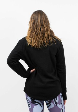 Schwarzes Fleece-Oberteil mit langen Ärmeln, lockerer Passform, abgerundetem Saum, gerippten Bündchen und glatter Textur, getragen mit gemusterten Leggings.