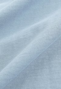 Svijetloplava tkanina s glatkom teksturom, koja ima suptilan rebrasti uzorak. Materijal pokazuje naborana i naborana svojstva.