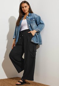 Jeansjacka i blått med knappar, vit linne, lätta svarta cargo-byxor med fickor och svarta sandaler med nitar.