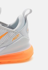 Ljusgrå sneaker med en andningsbar mesh-övre, orange detaljer, vadderad krage och en transparent orange dämpningssula.