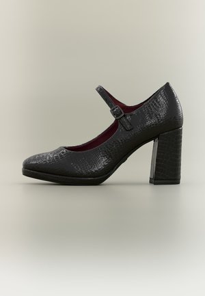 Zapato Mary Jane de charol negro con patrón texturizado, puntera redonda, tira ajustable y tacón bloque sobre fondo gris claro.