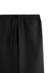Pantaloni neri con texture, dotati di un elastico in vita e di un cordoncino per la regolazione. Il tessuto presenta una superficie a trama sottile.