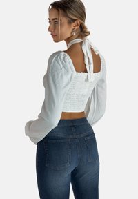 Hvid smocked crop top med udblæste ærmer og rygbinding, parret med tætsiddende mørk denim jeans med baglommer.