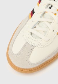 Superga z bež sintetičnim zgornjim delom in sivimi antilop dodatki, z večbarvnimi črtami, teksturiranimi vezalkami ter gumijastim podplatom barve gume.