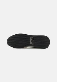 Svart gummisåle med sikksakkmønster, med en hvit Calvin Klein-logoetikett. Materialet ser slitesterkt og teksturert ut.