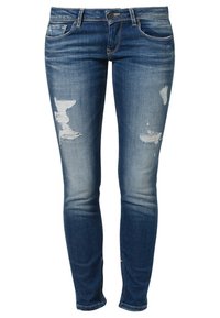 Jeans ajustados en denim azul oscuro, con detalles desgastados y grandes roturas, un estilo clásico de cinco bolsillos, cierre de botón y trabillas para el cinturón.