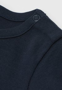 Námořnická modrá ribbovaná látka s kulatým výstřihem a kovovými patentkami na rameni. Hladká textura, přiléhavý střih.