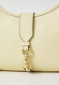 Κίτρινη δερμάτινη τσάντα με στρογγυλή μορφή, που διαθέτει χρυσαφένια μεταλλική λεπτομέρεια και ραφές κατά μήκος του λουριού.